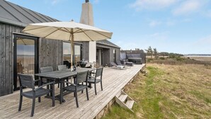 Une terrasse en bois avec des meubles d’extérieur, un barbecue et un grand parasol.