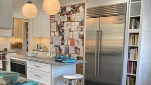 Eine moderne Küche mit einem Edelstahl-Kühlschrank, einer Marmorarbeitsplatte und einer Korkwand mit Notizen.