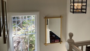 Eine Treppe mit weißer Geländer, ein schwarzer Laternenmast und ein Fenster mit Blick auf Bäume.