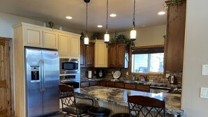 A kitchen with a stainless steel refrigerator, double ovens, a microwave, a sink, and a large island with bar stools.