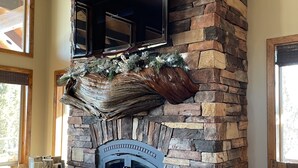 A stone fireplace with a TV mounted above it, surrounded by natural decor and a log fire.