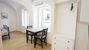 Ein Zimmer mit Holzboden, einem Bett mit Blumenmuster-Überwurf, einem Esstisch mit Stühlen und einer weißen Kommode mit Schubladen.