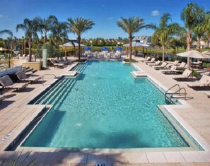 Une piscine rectangulaire à l’eau d’un bleu limpide, entourée de chaises longues et de parasols.