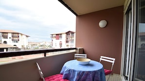Ein Balkon mit Tisch und Stühlen, eine rote gepolsterte Bank und Blick auf Gebäude im Hintergrund.