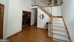 Un intérieur spacieux avec un escalier en bois, un coin repas et une cuisine visible à travers une porte ouverte.