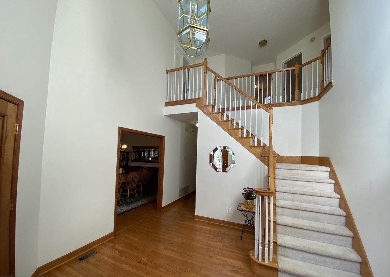 Un intérieur spacieux avec un escalier en bois, un coin repas et une cuisine visible à travers une porte ouverte.
