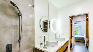 Un baño moderno con cabina de ducha de vidrio, dos lavamanos y un espejo.