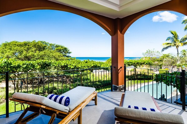 A balcony with two lounge chairs, a pool, and a view of the ocean.