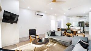 Una sala de estar moderna con un sofá, sillas, una mesa de centro, un televisor y una cocina al fondo.
