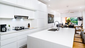 Cocina moderna con armarios blancos, una isla central, estufa integrada y un comedor con vistas a zonas verdes.
