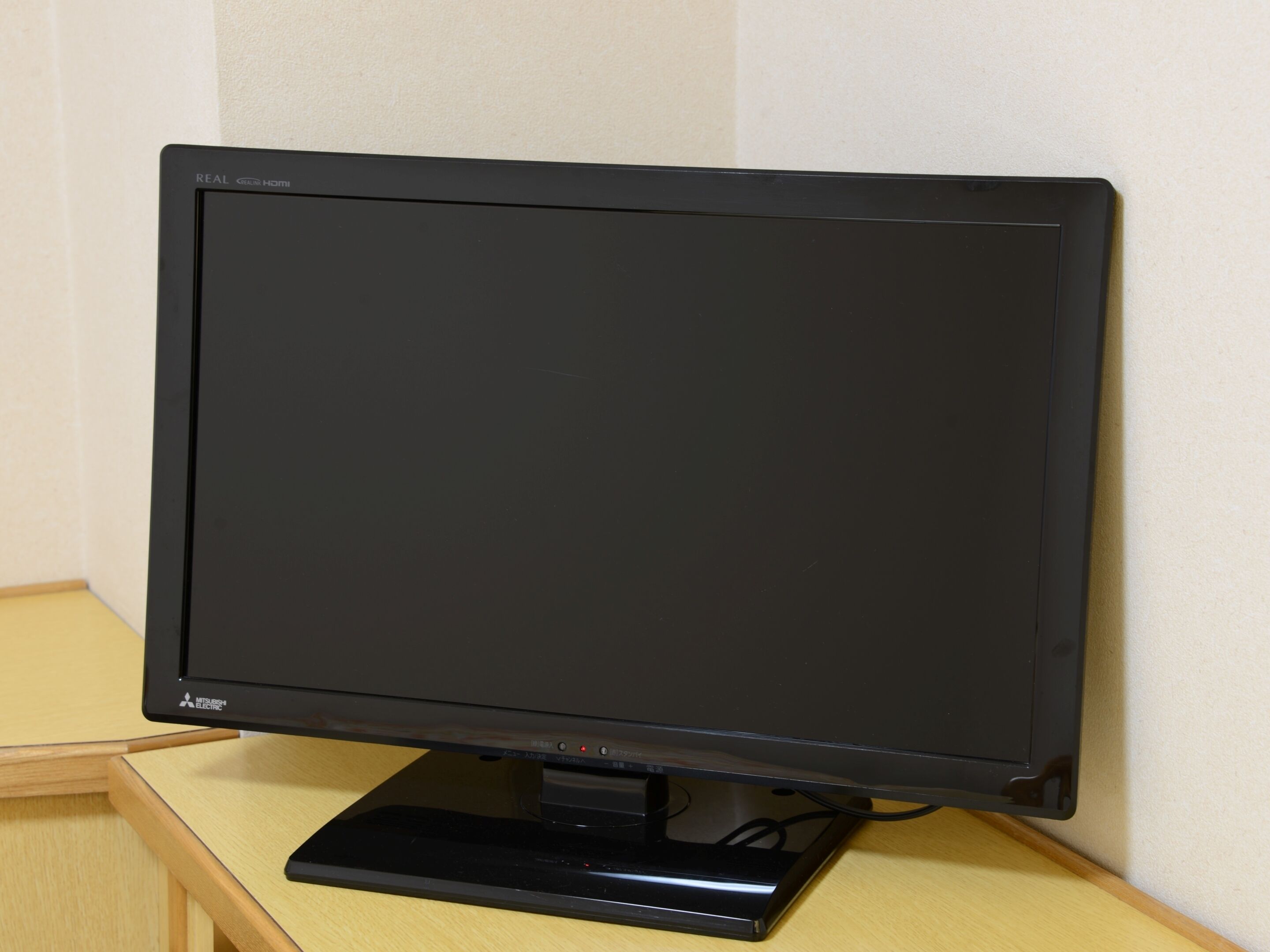 A flat-screen monitor with a stand, placed on a wooden table against a wall.