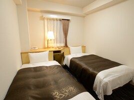 A hotel room with two beds, a desk, a lamp, and a telephone.