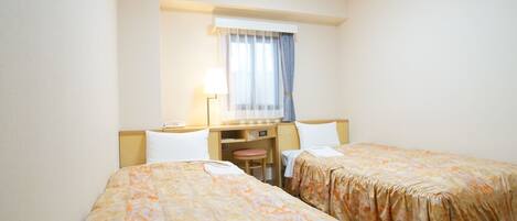 Una habitación de hotel con dos camas, un escritorio con silla, una lámpara y una ventana con cortinas.