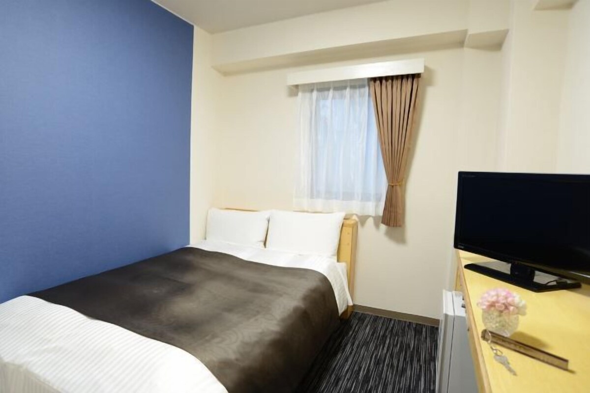 A hotel room with a bed, a TV, and a window with curtains.