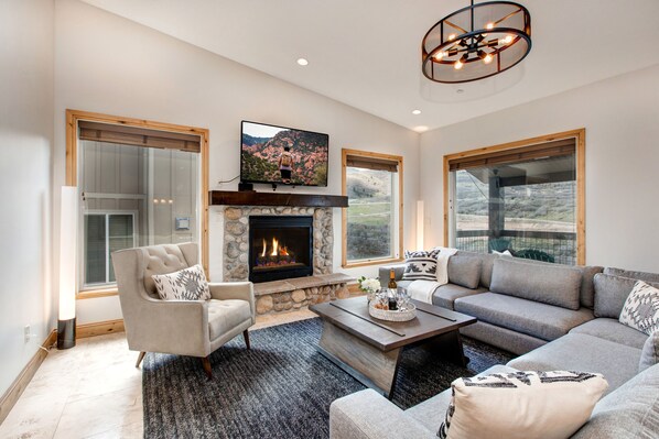 A living room with a stone fireplace, a large flat-screen TV, and a sofa. - Luxury Home in Great Location, Hot Tub + Patio, Family/Theater Room! (Heber City)