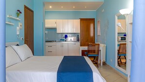 A bedroom with a bed, a desk with a chair, a kitchenette, and a bathroom. - Pippo House Beach Front (Giardini Naxos)