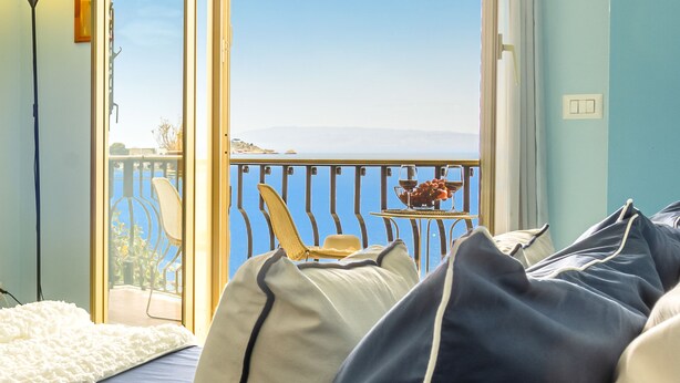 A bedroom with a view of the sea, a balcony with a chair, and a table with fruit. - Pippo House Beach Front (Giardini Naxos)
