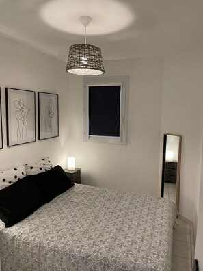 A bedroom with a bed, a bedside table with a lamp, a window, and wall art.