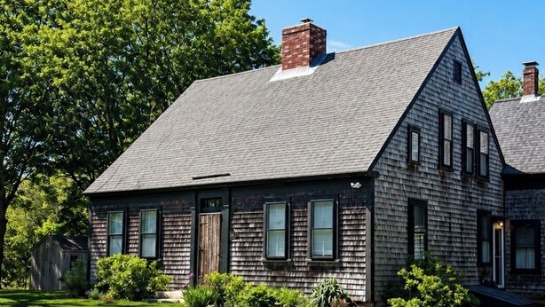 A two-story house with a sloped roof, a chimney, and a front porch.
