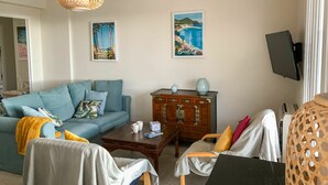 A living room with a blue sofa, a wooden cabinet, a coffee table, and a TV mounted on the wall. - Lovely apartment for 6 guests with WIFI, A/C, TV and terrace (Saint-cyr-sur-mer)