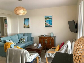 Ein Wohnzimmer mit blauem Sofa, einem Holzschrank, einem Couchtisch und einem an der Wand befestigten Fernseher.