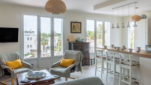 A spacious living area with a sofa, chairs, a coffee table, and a dining area with a bar. Large windows provide a view of the outside. - Lovely apartment for 6 guests with WIFI, A/C, TV and terrace (Saint-cyr-sur-mer)