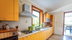 A kitchen with yellow cabinets, a gas stove, a microwave, and a window with a view of greenery. - Wonderful private villa for 10 people with private pool, WIFI, A/C, TV and terrace (Castellammare Del Golfo)