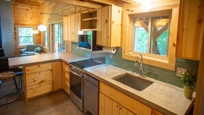 A wooden cabin kitchen with a central island, built-in oven, dishwasher, and a large window.