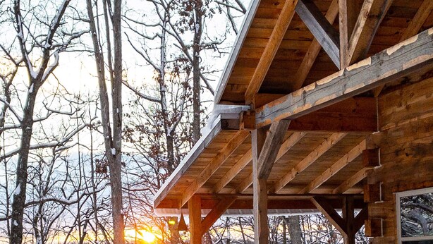 A wooden cabin with a covered porch and a staircase leading to a deck.