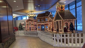 A hotel lobby with a large, illuminated gingerbread house display and a white picket fence.