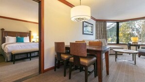 A hotel room with a bed, a dining table with chairs, a sofa, and a large window with a view of trees.