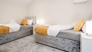 A modern bedroom with two beds, each with a grey headboard, white bedding, and a yellow pillow. - Cosy 2BR Maisonette near Hospital & Stations (Bedford)