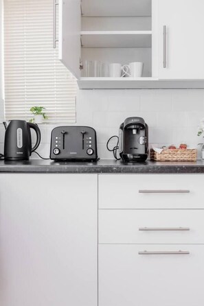 A kitchen with white cabinets, a black coffee maker, a toaster, and a kettle on the counter.