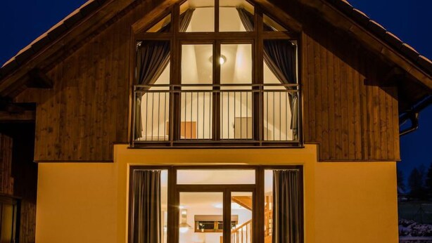 Una casa de madera de dos pisos con ventanas grandes y un balcón.