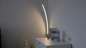Ein Nachttisch mit einem Buch mit dem Titel 'Welcome Book', einem kleinen Schild, einer Nachttischlampe und einer Vase mit weißen Blumen.