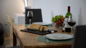 Ein Holztisch mit Brot, einer Weinflasche, einem Weinglas, einer Obstschale und einem weiteren Weinglas.