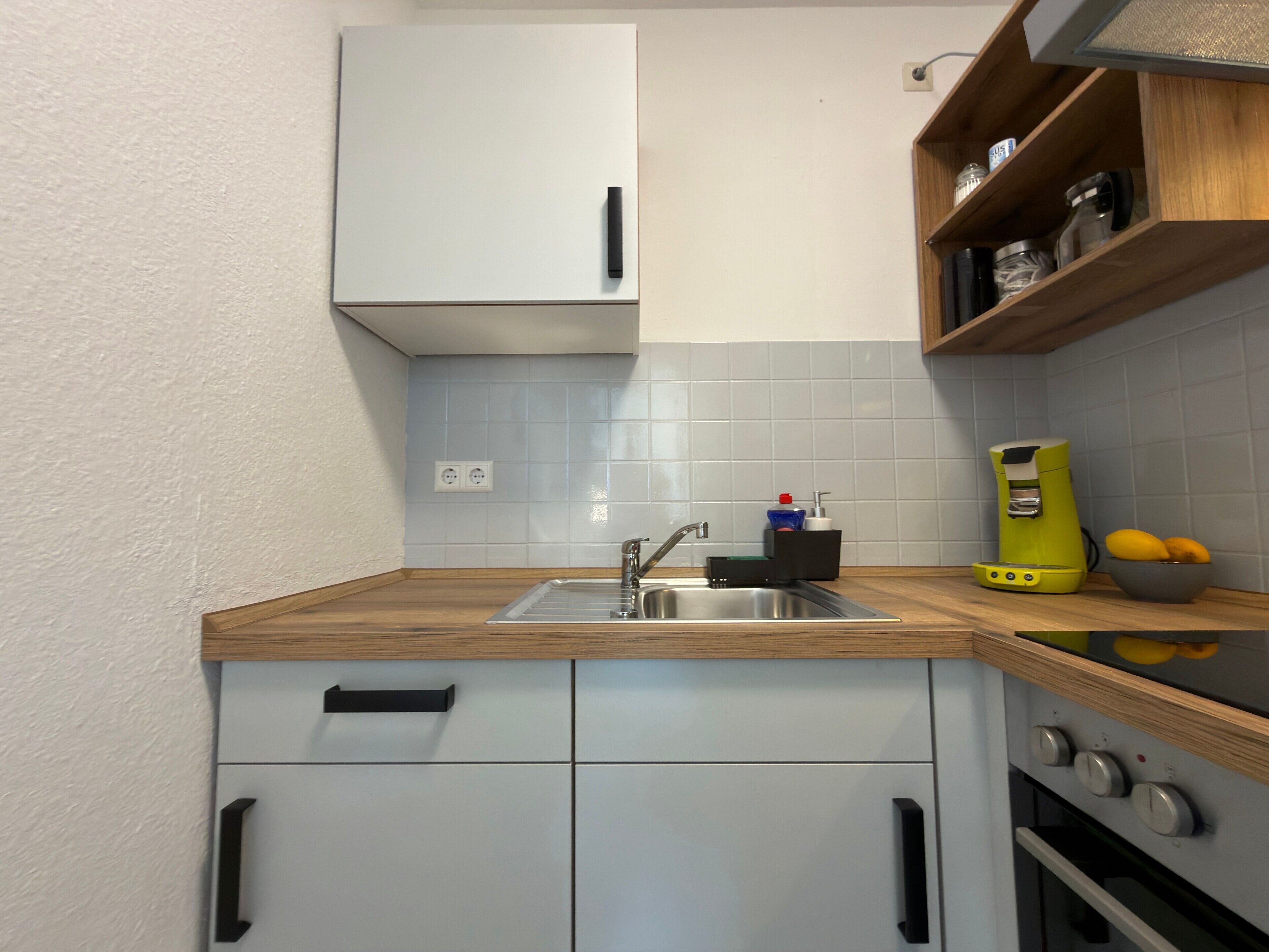 Una cocina con un lavamanos, una cafetera y un frutero.
