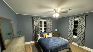 Een slaapkamer met een bed, nachtkastje, spiegel en plafondventilator.