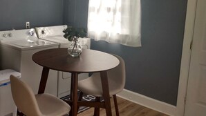 Een compacte keuken met een wasmachine, een eettafel met stoelen en een raam met dunne gordijnen.