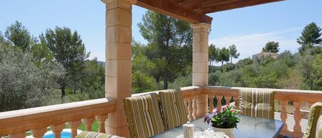 Un área de estar al aire libre cubierta con una mesa dispuesta para tomar té, rodeada de cojines a rayas, con vistas a una piscina y una colina.