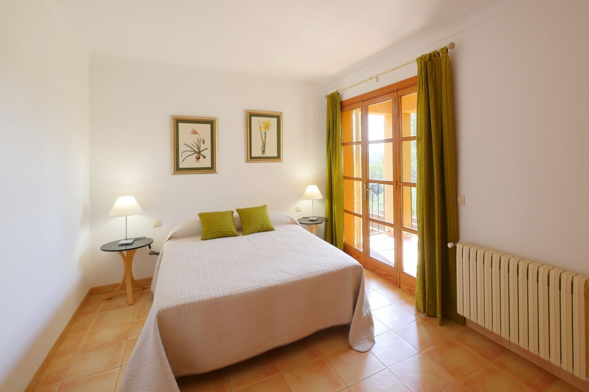 A bedroom with a bed, two bedside tables, a window with curtains, and two framed pictures on the wall.