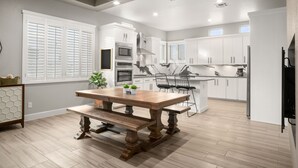 A modern kitchen with white cabinets, a wooden dining table, and a built-in island with seating. - Three Trees Saltwater Pool Place-Heated Pool (El Paso)