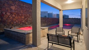 An outdoor patio with a stone wall, a hot tub, and a pool area with chairs and tables. - Three Trees Saltwater Pool Place-Heated Pool (El Paso)