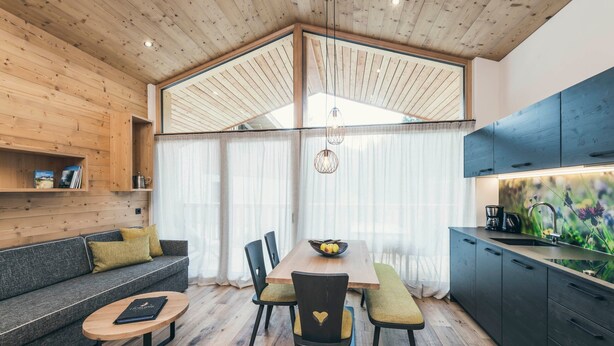 A modern interior with a wooden ceiling, a dining table with chairs, a sofa, and a kitchen area.
