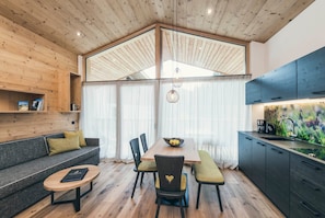 Un interior moderno con techo de madera, una mesa de comedor con sillas, un sofá y una zona de cocina.