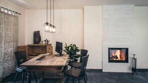 A dining area with a wooden table, chairs, a chandelier, a fireplace, and a plant.