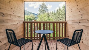 A wooden deck with a round table and two chairs, overlooking a forested landscape.