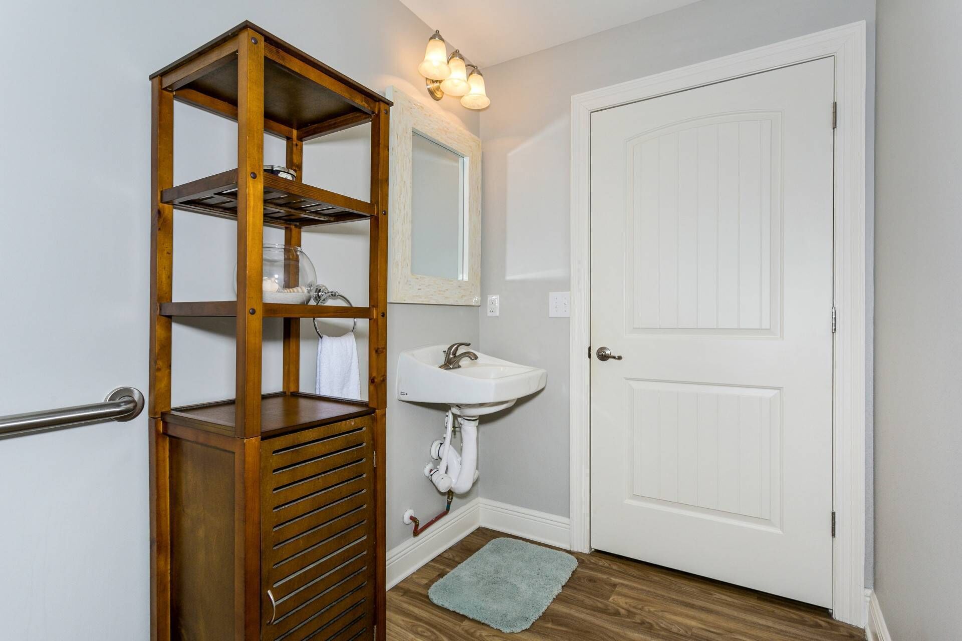 Een badkamer met een houten wandplank, een witte wastafel, een spiegel en een deur.