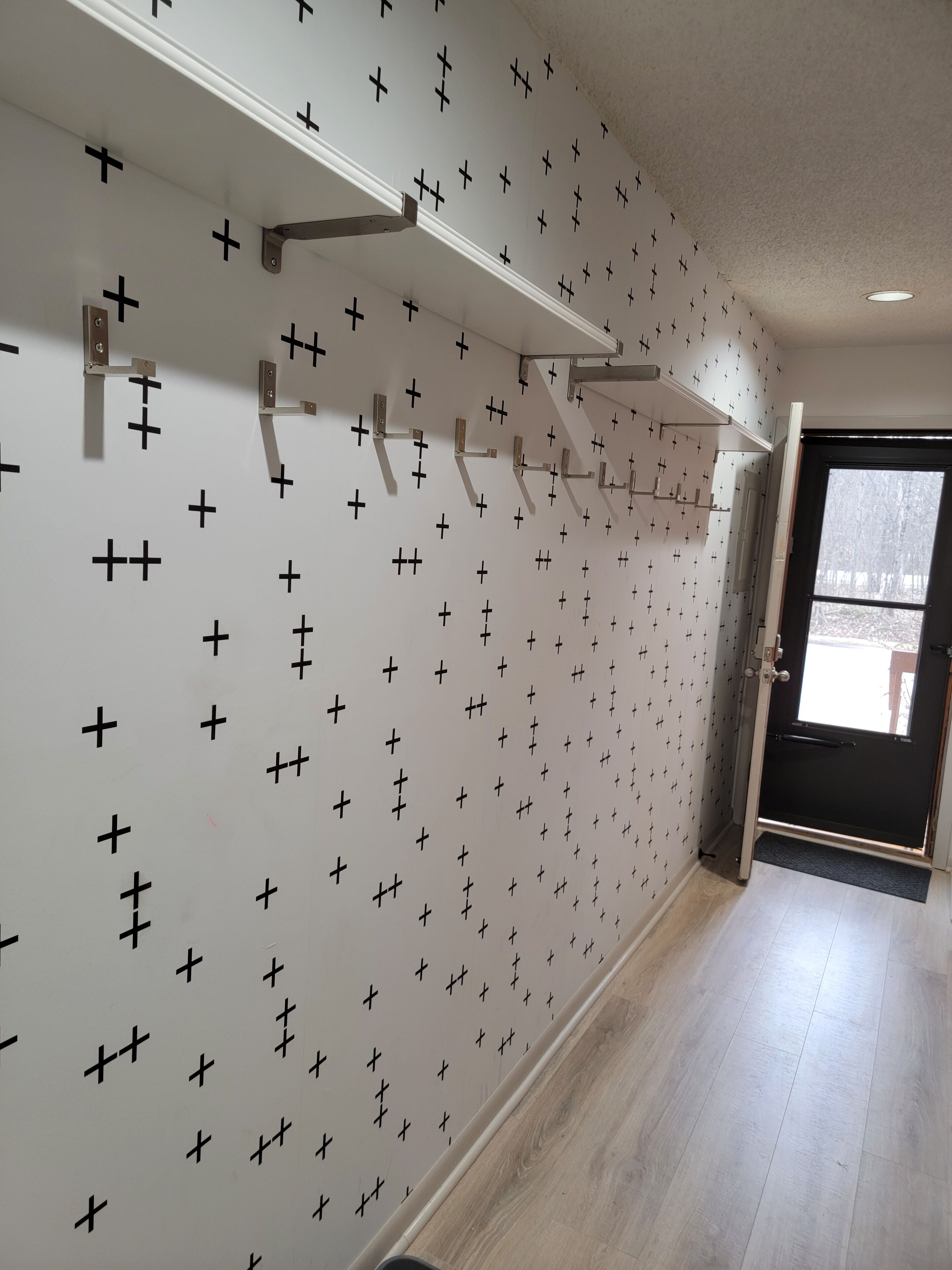 Un couloir avec un mur orné de motifs, une porte dotée d’une fenêtre et un luminaire fixé au plafond.