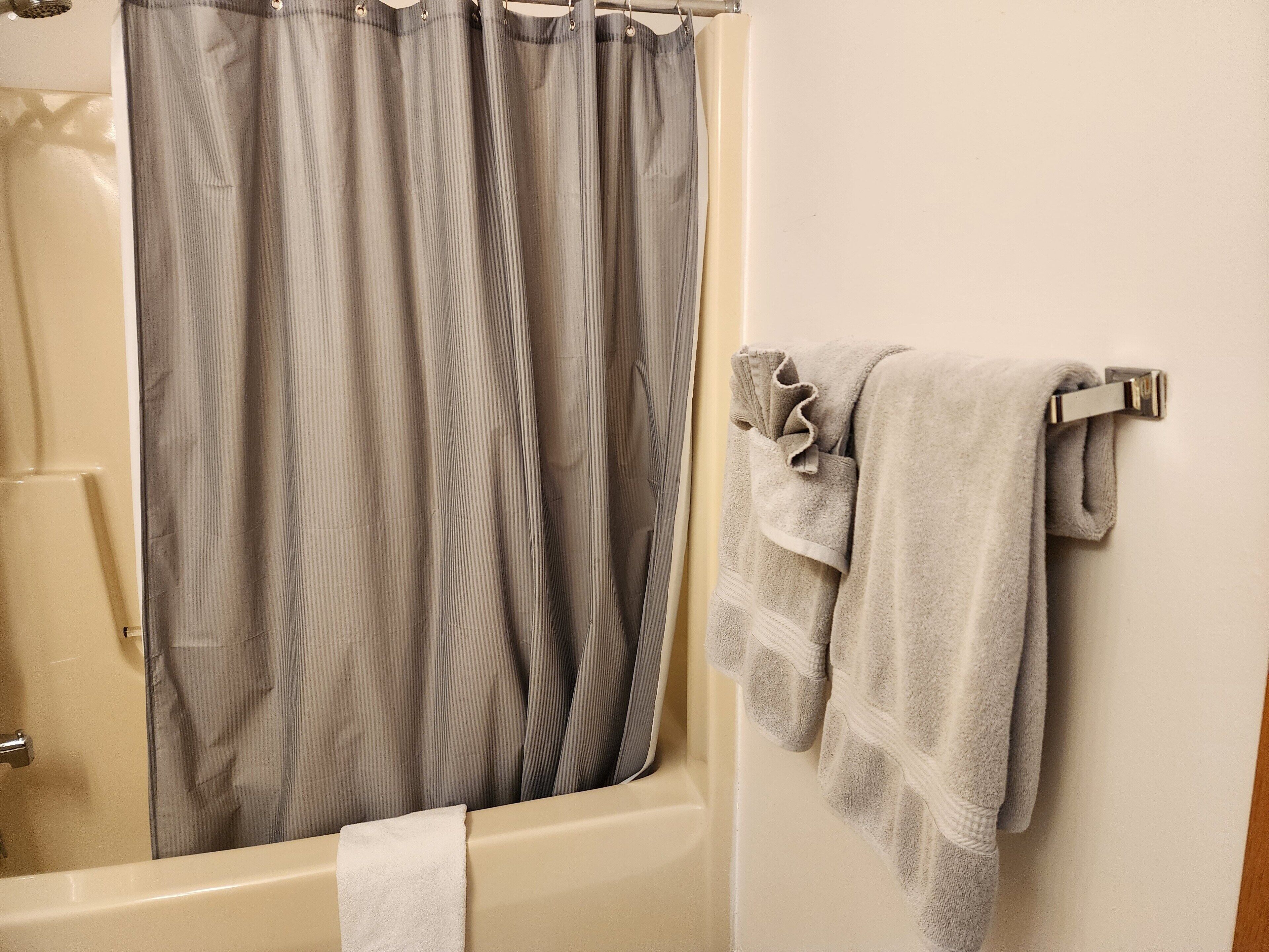 A bathroom with a bathtub, a shower curtain, and a towel rack with towels.